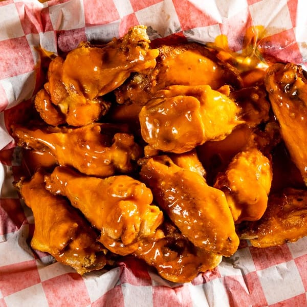 Close-up of a basket of golden-brown chicken wings coated in a glossy orange sauce, on red and white checkered paper.
