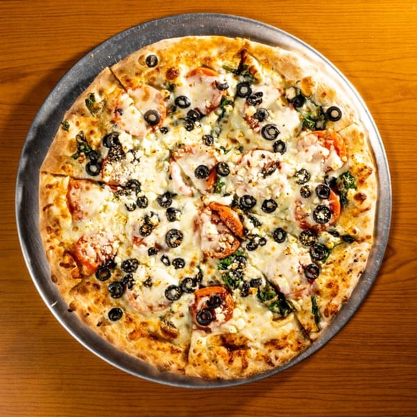 Whole pizza with tomatoes, black olives, spinach, and feta cheese on a metal pan.