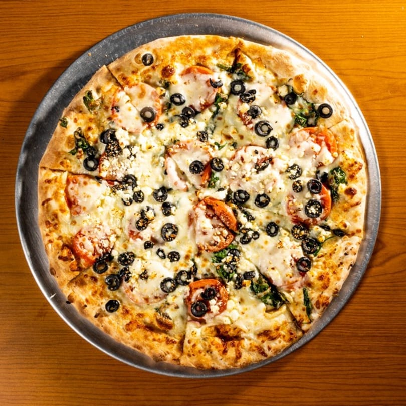 Whole pizza with tomatoes, black olives, spinach, and feta cheese on a metal pan.