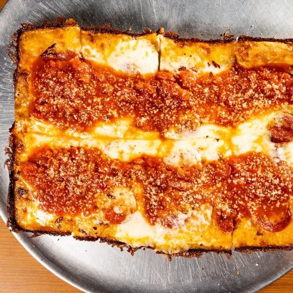 A rectangular Detroit-style pizza with thick crust, melted cheese, red sauce, and pepperoni on a metal pan.