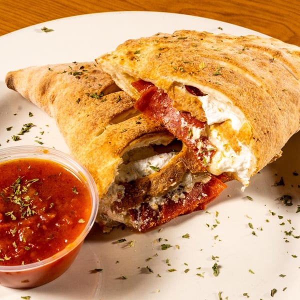 A golden-brown calzone, sliced open to reveal ricotta cheese and pepperoni, served with marinara sauce.