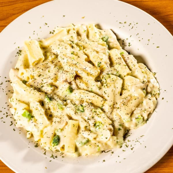 Creamy pasta with broccoli florets and black pepper on a white plate.