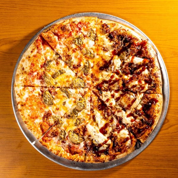 A large pizza with two distinct halves: one with red sauce and pesto, the other with BBQ chicken.