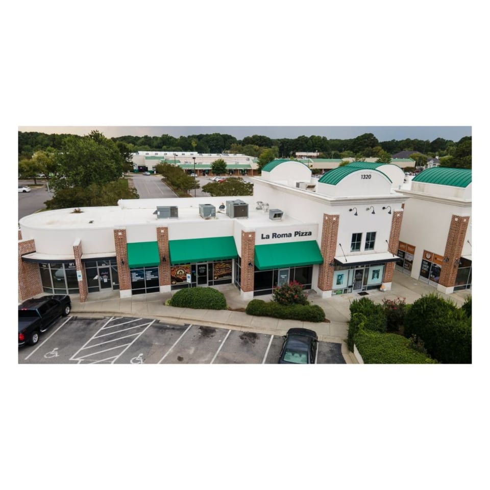 Aerial view of La Roma Pizza restaurant with green awnings in a strip mall with parking.