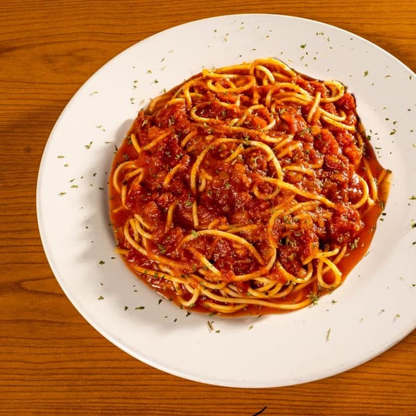 A white plate filled with spaghetti and a rich red tomato sauce, sprinkled with herbs.