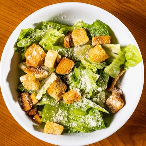 A white bowl filled with green lettuce, golden croutons, and grated cheese on a wooden table.