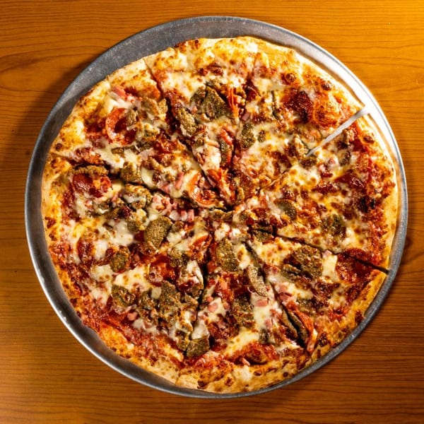 A whole meat lover's pizza with pepperoni, sausage, and ham, on a metal tray.